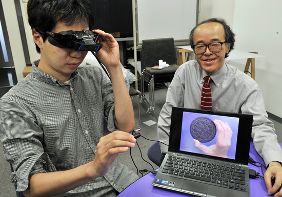 Tokyo, Tokyo, JAPAN: Tokyo University professor Michitaka Hirose (R) and his team developed a camera-equipped special goggle, which makes cookies bigger to help users diet at his laboratory in Tokyo on June 2, 2012. Hirose conducted an experiment, asking examinees to eat as many cookies as they want with and without the glasses. The results showed they ate 9.3 percent less on average with the goggle showing cookies 1.5 times bigger than they actually are and ate 15 percent more with cookies looking two-thirds of their real size. AFP PHOTO/Yoshikazu Tsuno