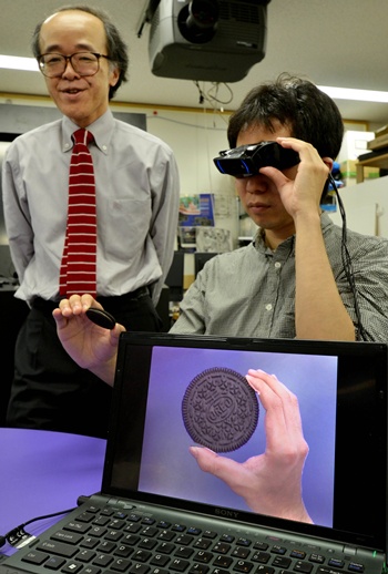 Tokyo, Tokyo, JAPAN: Tokyo University professor Michitaka Hirose (L) and his team developed a camera-equipped special goggle, which makes cookies bigger to help users diet at his laboratory in Tokyo on June 2, 2012. Hirose conducted an experiment, asking examinees to eat as many cookies as they want with and without the glasses. The results showed they ate 9.3 percent less on average with the goggle showing cookies 1.5 times bigger than they actually are and ate 15 percent more with cookies looking two-thirds of their real size. AFP PHOTO/Yoshikazu Tsuno