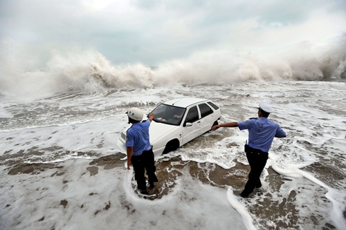 Qingdao, Shandong, CHINA: This picture taken on August 28, 2012, shows police trying to help remove a car surrounded by water after its owner parked it on the bank to watch waves brought on by Typhoon Bolaven in Qingdao, in northeast Chinas Shandong province. Typhoon Bolaven -- the strongest storm to hit South Korea for almost a decade -- left a trail of death and damage in southwestern and south-central regions of the Korean peninsula on August 28, and crossed into China early on August 29. AFP PHOTO