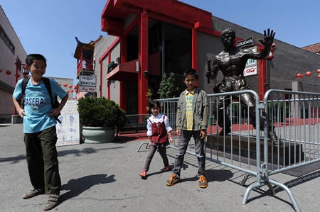 Los Angeles, California, UNITED STATES: Three young visitors pose in front of a new statue of the late martial arts icon Bruce Lee is seen in Chinatown in downtown Los Angeles June 16, 2013. The 7.6-feet (2.31 meters) tall bronze statue of the Hollywood legend was unveiled yesterday and will be on temporary display during the summer as organizers work to raise the additional US$150,000 needed to permanently install the statue. AFP PHOTO/Robyn Beck