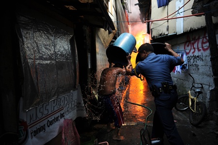 Manila, PHILIPPINES: A policeman (R) using a wash basin to protect himself from the heat as he persuades a resident to leave next to burning houses after a fire engulfed a shanty town at the financial district of Manila on July 11, 2013. There were no immediate reports of casualties from the blaze, which occurred mid-morning amid government plans to relocate thousands of families living in areas vulnerable to floods and typhoons. AFP PHOTO/Ted Aljibe