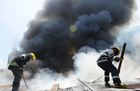 Manila, PHILIPPINES: Firemen remove a roof as they try to extinguish burning houses as a fire engulfs a shanty town at the financial district of Manila on July 11, 2013, leaving more than 1,000 people homeless according to city officials. There were no immediate reports of casualties from the blaze, which occurred mid-morning amid government plans to relocate thousands of families living in areas vulnerable to floods and typhoons. AFP PHOTO/Ted Aljibe