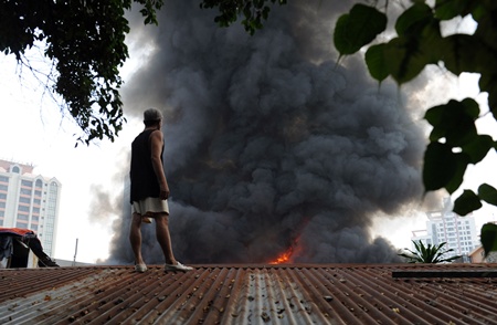 Manila, PHILIPPINES: A resident standing on the roof of his house looks at a fire engulfing a shanty town at the financial district of Manila on July 11, 2013, leaving more than 1,000 people homeless according to city officials. There were no immediate reports of casualties from the blaze, which occurred mid-morning amid government plans to relocate thousands of families living in areas vulnerable to floods and typhoons. AFP PHOTO/Ted Aljibe