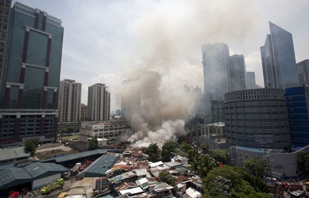 Manila, PHILIPPINES: Smoke rises after a fire engulfed a shanty town in the financial district of Manila on July 11, 2013. There were no immediate reports of casualties from the blaze, which occurred mid-morning amid government plans to relocate thousands of families living in areas vulnerable to floods and typhoons. AFP PHOTO/KarlMalakunas