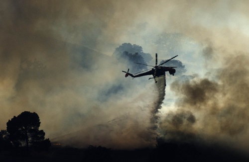 Los Angeles, California, UNITED STATES: A fire helicopter dumps water on a brush fire near Highway 101 and Calabasas on August 18, 2013 north of Los Angeles, California. A car fire sparked a brush fire off the northbound 101 Freeway in Calabasas on Sunday. LA County Fire says the blaze has burned between 40 to 50 acres. Crews are battling flames from the ground and air. AFP PHOTO/Joe Klamar