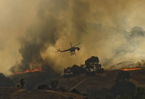 Los Angeles, California, UNITED STATES: A fire helicopter dumps water on a brush fire near Highway 101 and Calabasas on August 18, 2013 north of Los Angeles, California. A car fire sparked a brush fire off the northbound 101 Freeway in Calabasas on Sunday. LA County Fire says the blaze has burned between 40 to 50 acres. Crews are battling flames from the ground and air. AFP PHOTO/Joe Klamar
