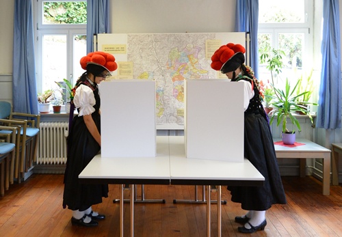 Hornberg-Reichenbach, Baden-Wurttemberg, GERMANY: Voters Gerlinde Moser (L) and Corinna Wohrle (R) wear a Black Forest traditional clothes and the pom-poms hat Bollenhut as they cast their ballot at a polling station on September 22, 2013 in Hornberg-Reichenbach, south-western Germany, the day of the German general elections. 