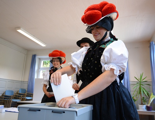 Hornberg-Reichenbach, Baden-Wurttemberg, GERMANY: (LtoR) Voters Gerlinde Moser, Christoph Wohrle and Corinna W?hrle wear Black Forest traditional clothes and the pom-poms hat Bollenhut as they queue to cast their ballot at a polling station on September 22, 2013 in Hornberg-Reichenbach, south-western Germany, the day of the German general elections. AFP PHOTO/DPA/Patrick Seeger 