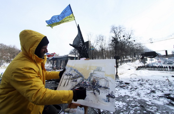 ศิลปินคนหนึ่งวาดภาพฉากเหตุการณ์ในเมืองหลวงของยูเครน ขณะที่ผู้ประท้วงต่อต้านรัฐบาลรวมตัวกันปิดถนน (ด้านหลังทางซ้าย) คนละฟากกับแถวของตำรวจปราบจลาจล ที่บริเวณใจกลางกรุงเคียฟเมื่อวันพุธ (29)