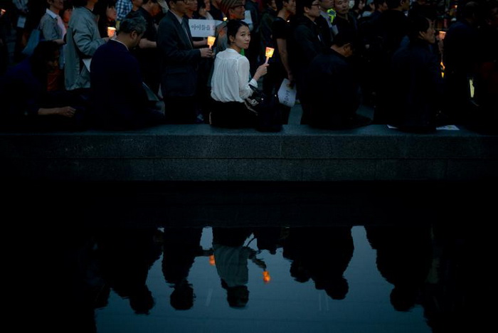 สตรีชาวเกาหลีใต้ถือเทียนไข ในเวลาที่ผู้ชุมนุมมาร่วมตัวกันเพื่อรำลึกถึงเหยื่อผู้เสียชีวิต และผู้สูญหายในเหตุเรือเฟอร์รี เซวอล อับปาง