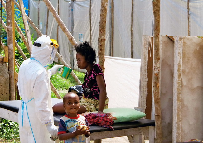 เจ้าหน้าที่สาธารณสุขซึ่งสวมเครื่องป้องกันนำน้ำดื่มไปให้แก่สตรีที่ติดเชื้ออีโบลา ภายในโรงพยาบาลเกเนมา จังหวัดอีสเทิร์นโปรวินซ์ เซียร์ราลีโอน (แฟ้มภาพ)