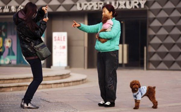 หญิงคนหนึ่งกำลังถ่ายรูปกับน้องหมาของเธอหน้าห้างสรรพสินค้าในกรุงปักกิ่ง – รอยเตอร์ 