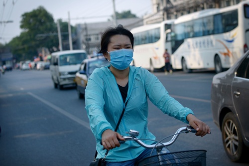 Beijing, CHINA: This picture taken on June 15, 2015 shows a woman wearing a face mask as she rides an electric bicycle along a street in Beijing. AFP PHOTO/Wang Zhao