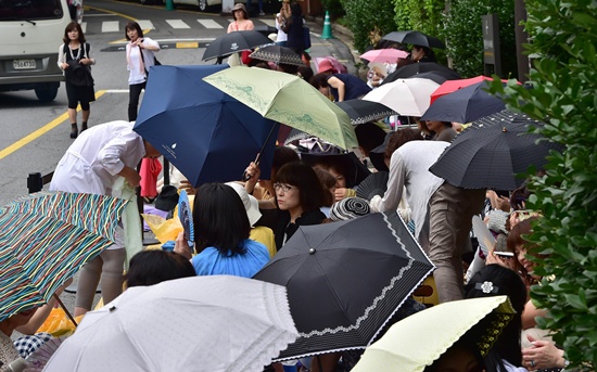 SEOUL, REPUBLIC OF KOREA: Japanese fans of South Korean actor Bae Yong-Joon holding umbrellas wait on a side of the road leading to the wedding hall to get a glimpse of their favorite star before Baes wedding ceremony at a hotel in Seoul on July 27, 2015. Scores of middle-aged Japanese women converged on a major Seoul hotel on July 27, hoping for a glimpse of their favourite South Korean TV drama star on his wedding day. AFP PHOTO/Jung Yeon-Je
