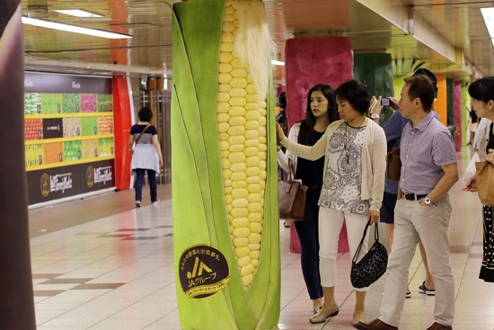 Tokyo, Tokyo, JAPAN: Pedestrians look at a large corn decoration cover at a underground passage of a subway station in Tokyo on September 2, 2015. Japan Agriculture Cooperative decorated the pillars of the underground passage with vegetable shaped covers such as radish, carrot, corn, cucumber, eggplant and sweet potato for the promotion of the domestically produced vegetables. AFP PHOTO/Yoshikazu Tsuno