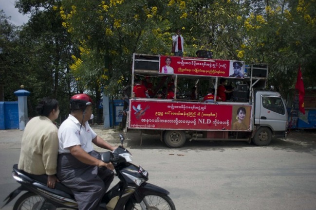 <br><FONT color=#000033>ชาวพม่าขี่รถจักรยานยนต์ผ่านรถรณรงค์หาเสียงของพรรค NLD ในเมืองตองจี ของรัฐชาน.--Agence France-Presse/Ye Aung Thu.</font></b>