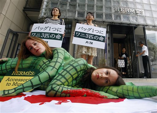 FILE - In this July 30, 2015 file photo, activists of People for the Ethical Treatment of Animals (PETA) perform with their bodies painted to look like slaughtered crocodiles in front of a Hermes shop ain Tokyos Ginza shopping district. The banners read  It takes three crocodiles to make one handbag. (AP Photo/Shizuo Kambayashi, File)