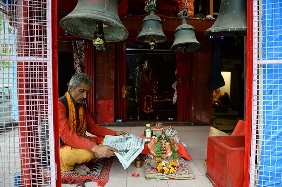 New Delhi, INDIA: In this photograph taken on November 26, 2015, an Indian priest reads a Sanskrit newspaper as he sits inside a temple in New Delhi. Sanskrit, the 4,000 year-old classical language, was traditionally used by Brahmin intellectuals and Hindu priests. Rarely spoken as a mother tongue in India, Sanskrit is often dismissed as a dead language. AFP PHOTO/Sajjad Hussain