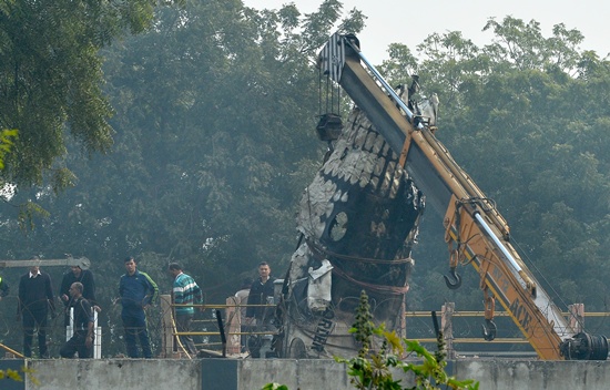 NEW DELHI, INDIA: A piece of plane wreckage is hoisted by a crane as rescue personel look on at the crash site of a chartered army plane close to the main airport in New Delhi on December 22, 2015. AFP PHOTO/Chandan Khanna