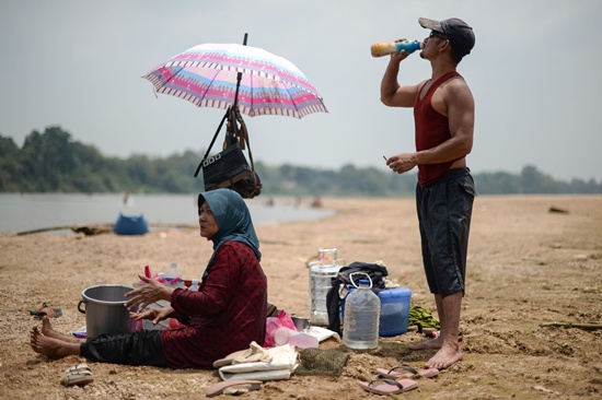 Temerloh, Malaysia: A man (R) drinks water along the dry banks of the Pahang river as schools remain closed due to the ongoing heatwave in Termerloh, outside Kuala Lumpur, on April 11, 2016. More than 250 Malaysian schools were closed on April 11 due to a heatwave brought on by the El Nino weather phenomenon which is severely affecting food production and causing chronic water shortages in many countries. AFP/Mohd Rasfan