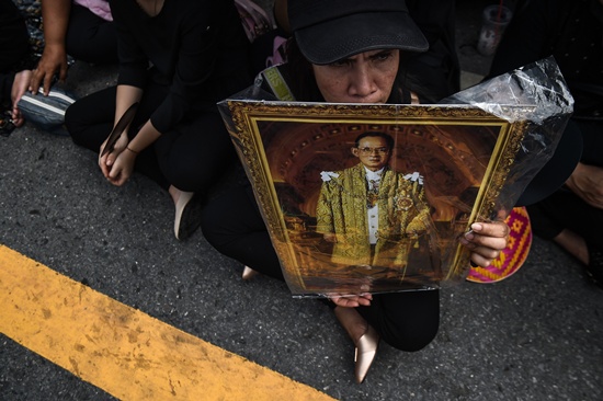 Bangkok: A mourner clad in black sits on the road with an image of the late Thai King Bhumibol Adulyadej in front of the Grand Palace in Bangkok on October 22, 2016. Thailands King Bhumibol Adulyadej died at the age of 88 on October 13 after years of ill health, ending a seven-decade reign and leaving the politically divided nation without its key pillar of unity. AFP/Lillian Suwanrumpha