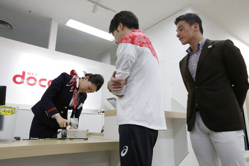 A store clerk scraps an old mobile phone watched by Japanese Olympic swimmer Takeshi Matsuda, right, and Paralympian Takuro Yamada at a shop of NTT Docomo, Japans mobile phone operator, in Tokyo, Saturday, April 1, 2017. Organizers of the 2020 Tokyo Olympics began Saturday collecting discarded electronic devices that will be used in the production of the medals to be awarded to athletes. The organizing committee aims to collect eight tons of raw metal which will yield around two tons of pure metal, enough to produce 5,000 medals for the Tokyo Games. (AP Photo/Eugene Hoshiko)