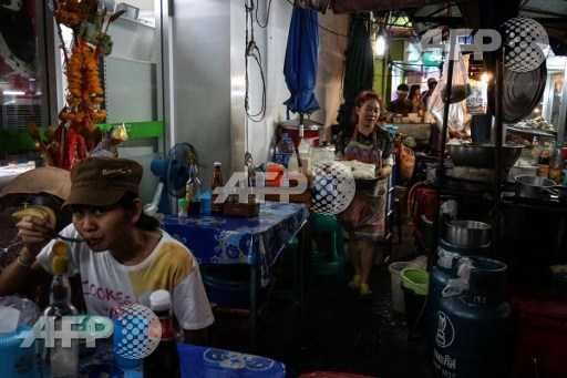 This photo taken on April 17, 2017 shows a woman working at a street noodle stall as a customer eats in the Phrakanong district of Bangkok. Street food stalls will be banned from all of Bangkoks main roads under a clean-up crusade, a city hall official said Tuesday, prompting outcry and anguish in a food-obsessed capital famed for its spicey roadside cuisine. Lillian Suwanrumpha/AFP