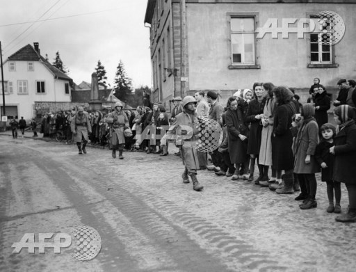 Picture released on November 25, 1944 of civilians of Lutzelhouse lining edge of the streets as American soldiers advance through the town, during the Second World War. US Army/AFP