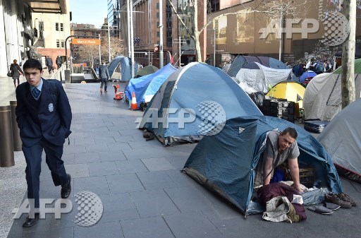 A homeless man (R) wakes up in his tent in Martin Place, which has become known as Tent City, in the central business district of Sydney on August 11, 2017. A homeless tent city in the heart of Sydney was being dismantled on August 11, after political wrangling over who was responsible for the plight of those sleeping rough in the midst of winter sparked the introduction of new laws. Peter Parks/AFP