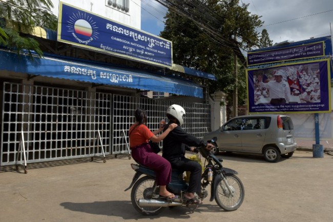ชาวเขมรขี่รถจักรยานยนต์ผ่านอาคารสำนักงานใหญ่พรรคกู้ชาติกัมพูชา (CNRP) ในกรุงพนมเปญ หลังศาลสูงตัดสินยุบพรรค. -- Agence France-Presse/Tang Chhin Sothy.