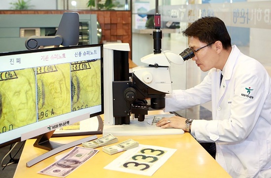 This undated handout photo provided by South Koreas KEB Hana Bank on December 12, 2017 shows Yi Ho-Joong, head of the KEB Hana Banks anti-counterfeit centre, inspecting a fake $100 banknote at the bank in Seoul. A new high-quality counterfeit $100 bill has been found in South Korea, bank officials said on December 12, prompting suggestions the sanctions-hit North might have resumed forging supernotes. handout/KEB Hana Bank/AFP