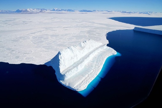 This NASA image released on December 20, 2017 and aquired on November 29, 2017 by Operation IceBridge during a flight to Victoria Land, shows an iceberg floating in Antarcticas McMurdo Sound. The part of the iceberg below water appears bluest primarily due to blue light from the water in the Sound. The undersides of some icebergs can be eroded away, exposing older, denser, and incredibly blue ice. Erosion can change an iceberg’s shape and cause it to flip, bringing the sculpted blue ice above the water’s surface. The unique step-like shape of this berg—compared to the tabular and more stable berg in the top-right of the image—suggests that it likely rotated sometime after calving. Chris Larsen/NASA/AFP
