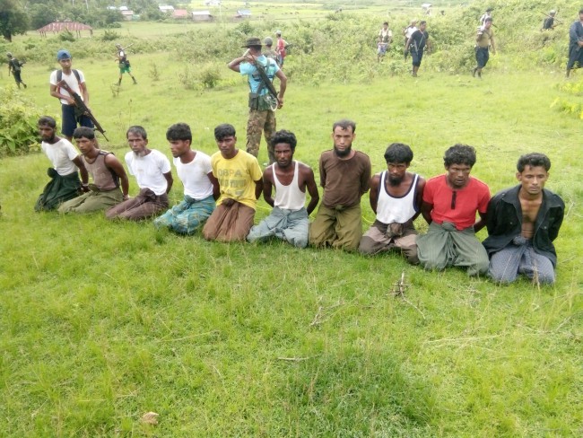 ชายชาวมุสลิมโรฮิงญา 10 คน ถูกมัดถือนั่งคุกเข่ากับพื้นขณะที่สมาชิกกองกำลังรักษาความมั่นคงพม่ายืนเฝ้าอยู่โดยรอบในหมู่บ้านอินดิน วันที่ 2 ก.ย 2560. -- Reuters.