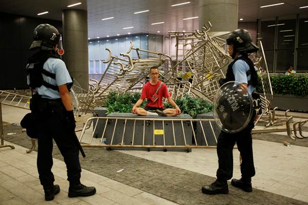 เจ้าหน้าที่ตำรวจยืนเฝ้าผู้ประท้วงที่นั่งประท้วงต่อต้านกฎหมายส่งตัวผู้ร้ายข้ามแดนไปจีนเมื่อคืนวันที่ 10 มิ.ย. 2019 (ภาพ รอยเตอร์ส)