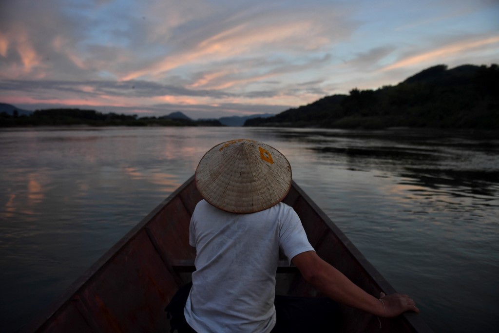ชายบนเรือประมง ในแม่น้ำโขง โดยฝั่งขวาคือ บริเวณ อ.สังคม จ.หนองคาย และฝั่งซ้ายคือลาว (LILLIAN SUWANRUMPHA / AFP)