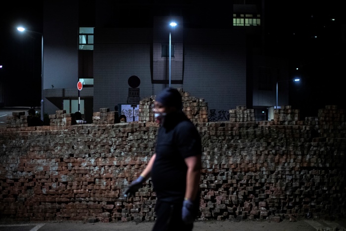 <i>ผู้ประท้วงเดินผ่านกำแพงซึ่งพวกเขานำเอาอิฐปูทางเท้าที่แงะออกมาสร้างขึ้น เพื่อใช้สกัดกั้นในเวลาตำรวจบุกเข้ามา ณ มหาวิทยาลัยจีน (CUHK) วันพุธ (13 พ.ย.) </i>
