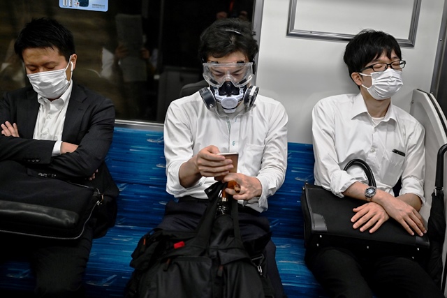 ชาวญี่ปุ่นคนหนึ่งสวมหน้ากากและแว่นตาป้องกันเต็มพิกัด ระหว่างโดยสารรถไฟในกรุงโตเกียว