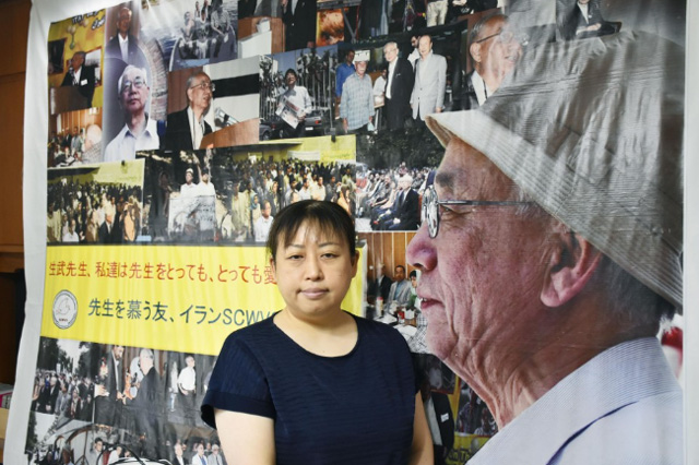 โนริโกะ ลูกสาวคนโตของหมอมาซาโตะ ยูกุทาเกะ ยืนอยู่หน้าแผงภาพถ่ายของเขาที่บ้านของเธอในมิฮาระ ฮิโรชิมา เมื่อวันที่ 3 ส.ค.2022 (ภาพเกียวโด)