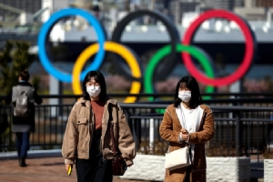 ผู้คนสวมหน้ากากอนามัยเดินอยู่หน้าวงกลม 5 วงสัญลักษณ์กีฬาโอลิมปิก ในกรุงโตเกียว   ทั้งนี้ไวรัส “โควิด-19” ที่ทำท่าระบาดรุนแรงขึ้นในญี่ปุ่น กำลังทำให้เกิดคำถามว่ามหกรรมกีฬาโอลิมปิกโตเกียว 2020 จะยังสามารถจัดขึ้นตามกำหนดเดิมได้หรือไม่